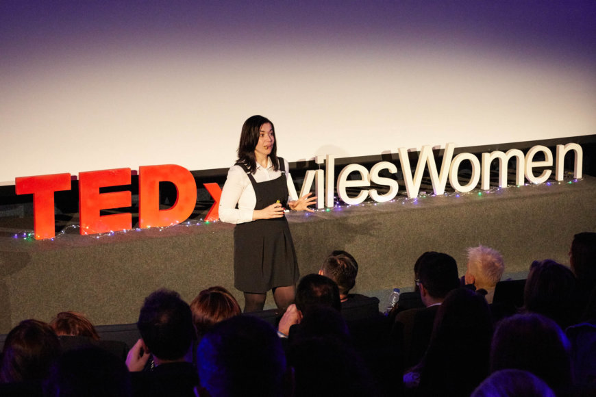 Mujer dando una charla en el escenario de TEDxAvilesWomen frente a un público atento.